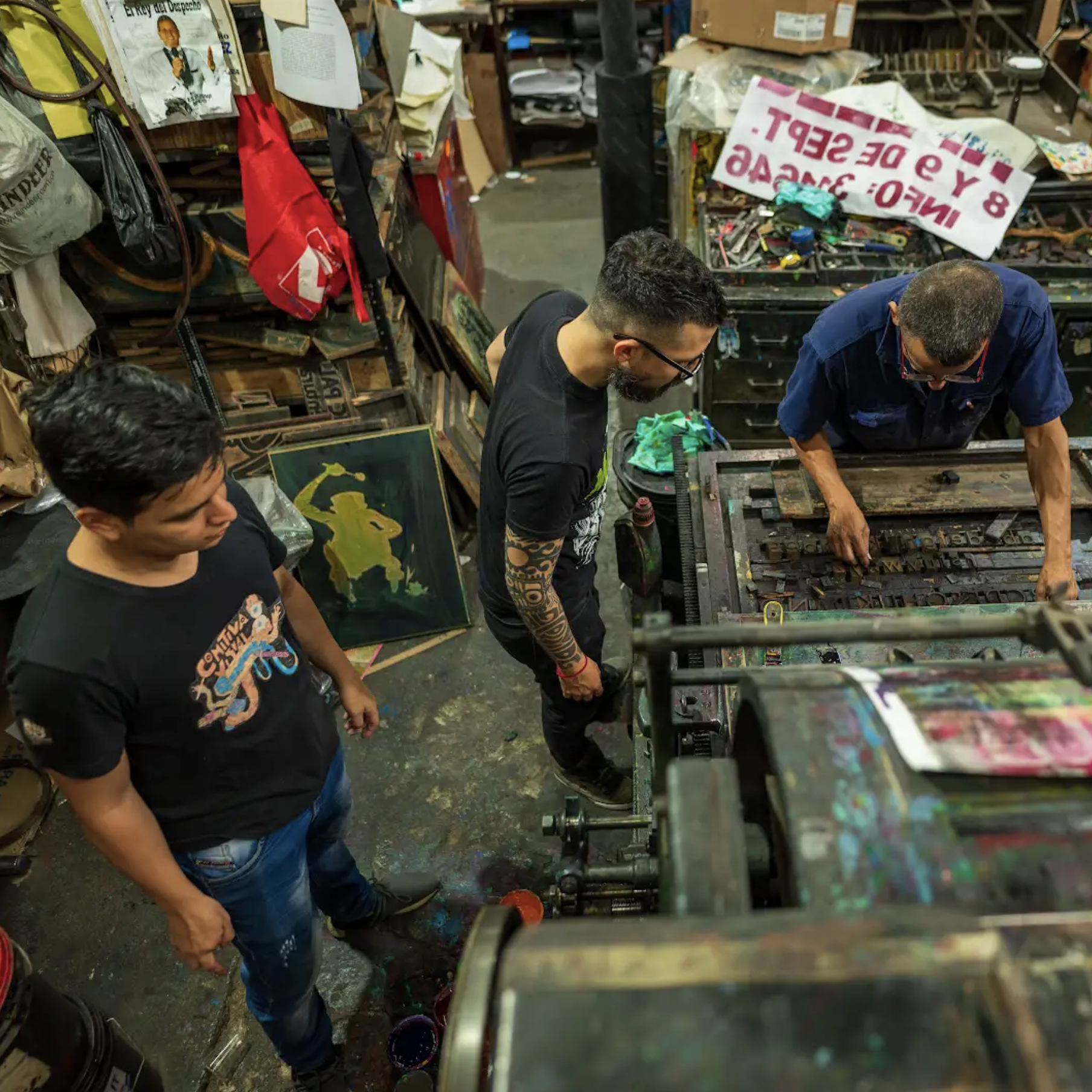 A group of several men look over a working printing press